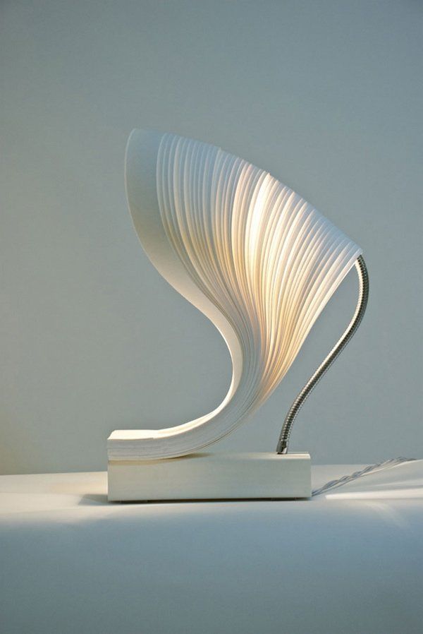 a white sculpture sitting on top of a table next to a light bulb in the shape of a wave