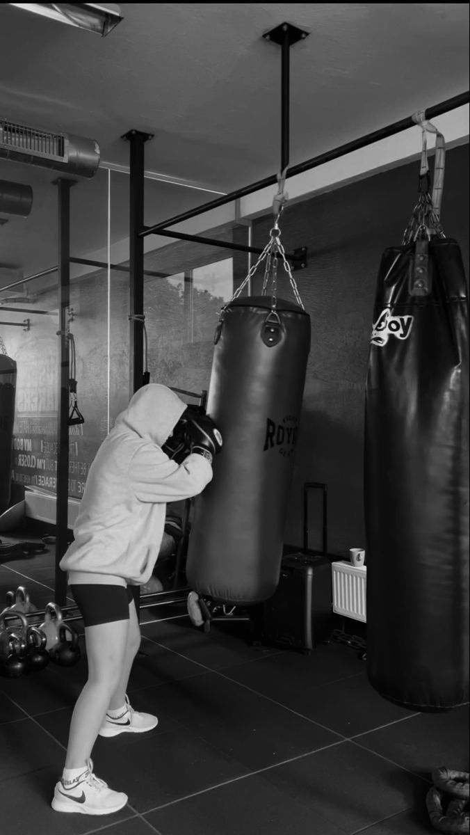 a woman in white shirt and black shorts standing next to punching bag on floor with other boxing equipment