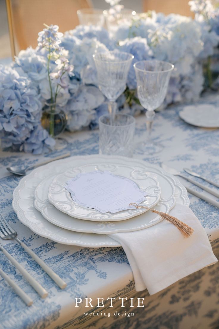 the table is set with plates, silverware and blue hydranges on it