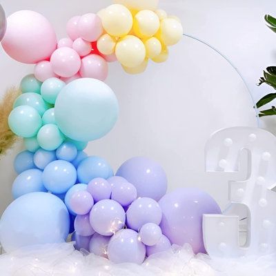 balloons are arranged in the shape of a rainbow on a white background with letters and plants