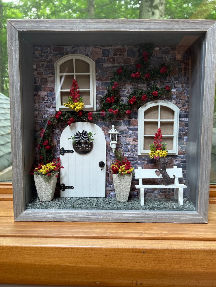 a miniature house with flowers and potted plants on the front door window sill