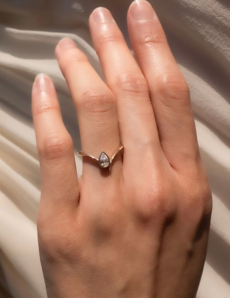 a woman's hand with a diamond ring on top of her left hand and white fabric in the background