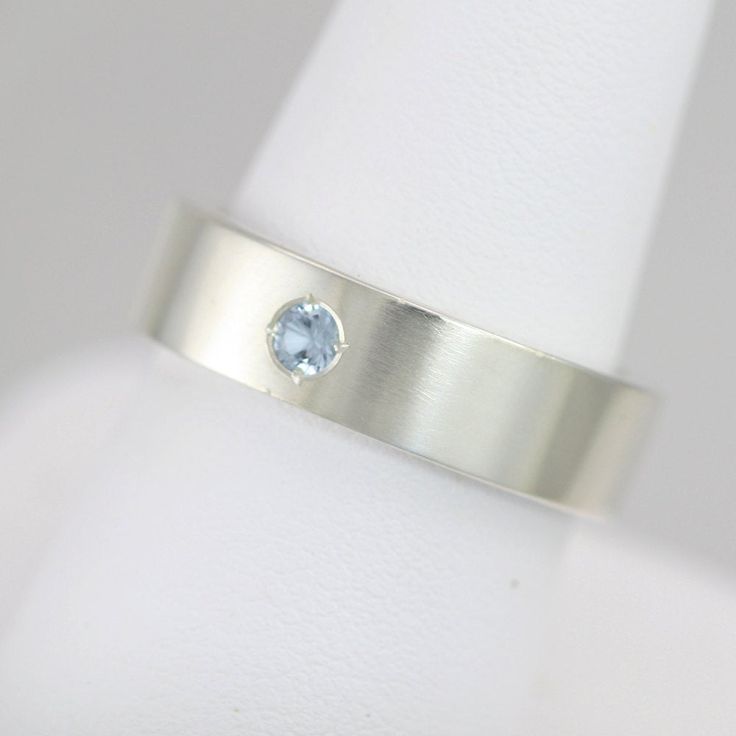 Handcrafted sterling silver ring with your choice of birthstone (Aquamarine pictured). Ring is 6mm wide and 2mm thick and has a 3mm round faceted lab-grown birthstone flush set in the center. The piece is brought to a glossy finish. This item is made to order, please allow up to 10 business days for fabrication. All stones are lab-grown except for Garnet, Amethyst, Peridot, and Citrine. Feel free to ask me for a price quote for any natural stone. Aquamarine Birthstone Ring In Round Cut, Silver Aquamarine Birthstone Ring With Prong Setting, Rectangular Aquamarine Ring For Gift, Round Aquamarine Gemstones As Gifts, Silver-tone Aquamarine Diamond Ring For Gift, Pearl Drop Pendant, Family Rings, Mother Rings, Wide Rings