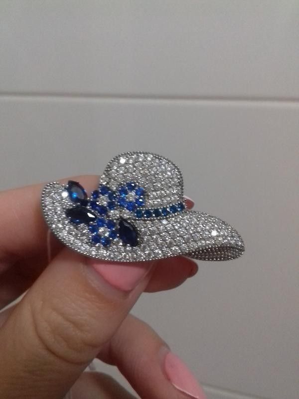 someone is holding a hat brooch with blue and white crystals on it in their hand