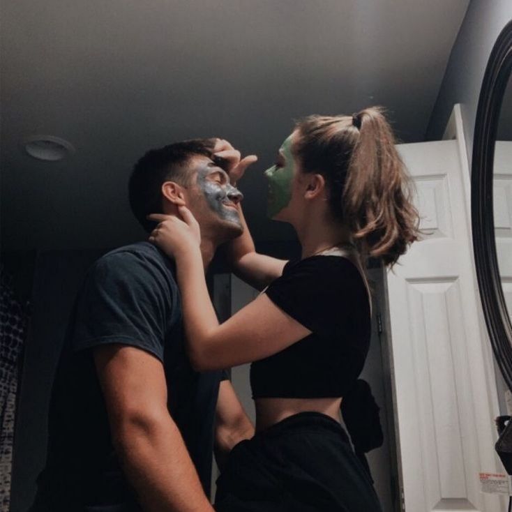 a man and woman standing in front of a mirror with their faces painted like they are kissing