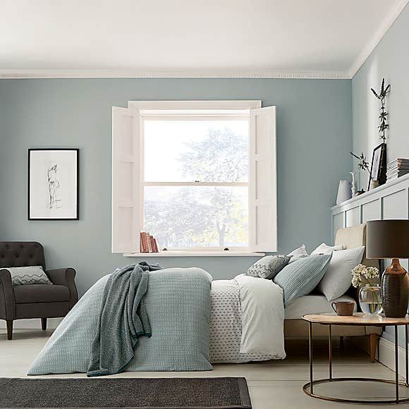 a bedroom with light blue walls and white trim on the windowsill, bed in foreground