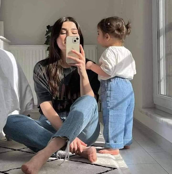 a woman sitting on the floor taking a photo with her phone while holding a toddler