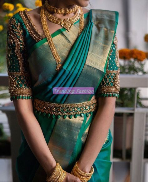 a woman in a green sari with gold jewelry on her neck and hands behind her back