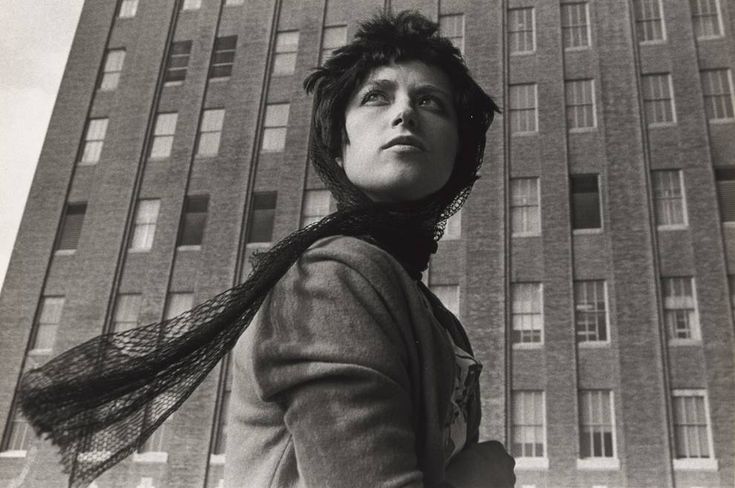 a black and white photo of a woman in front of a tall building with her hair blowing in the wind