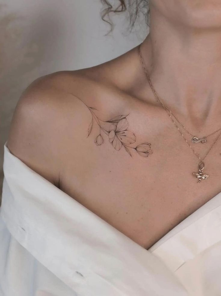 a woman with a tattoo on her chest is wearing a white dress and holding a necklace