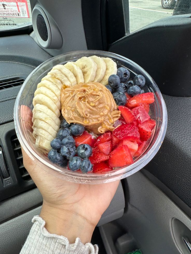 a person holding up a plastic bowl filled with fruit and peanut butter on top of it