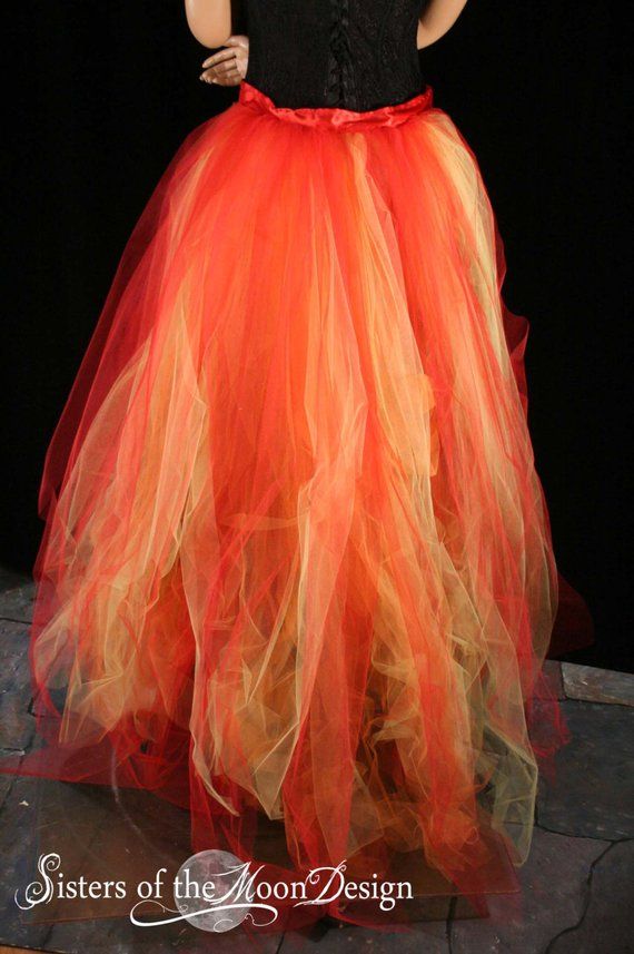 a woman wearing a black and orange dress with red trims on the bottom, standing in front of a dark background