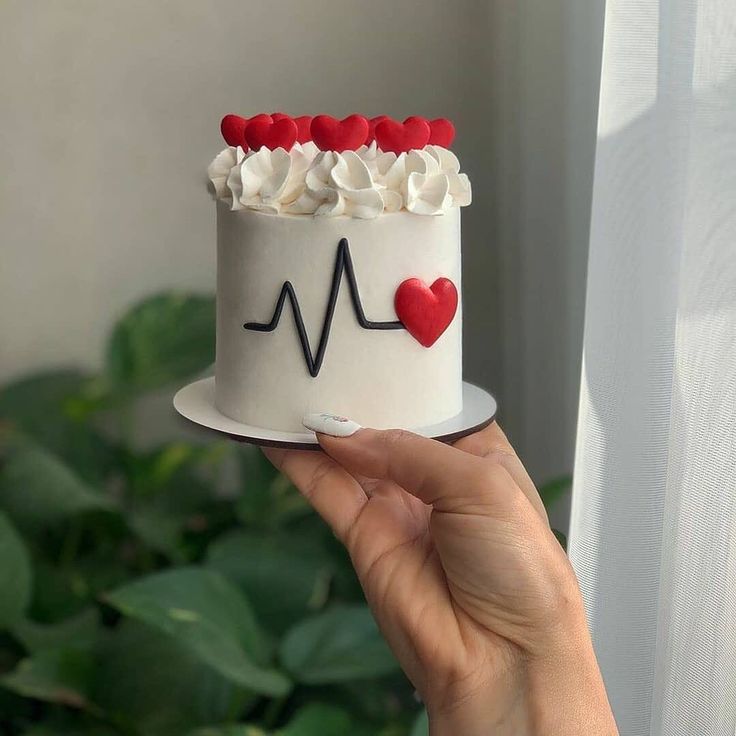 a woman holding a cake with white frosting and red hearts on it