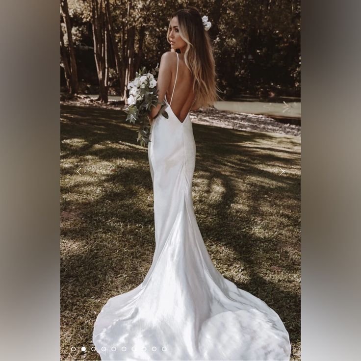 a woman in a white wedding dress standing on the grass with her back to the camera