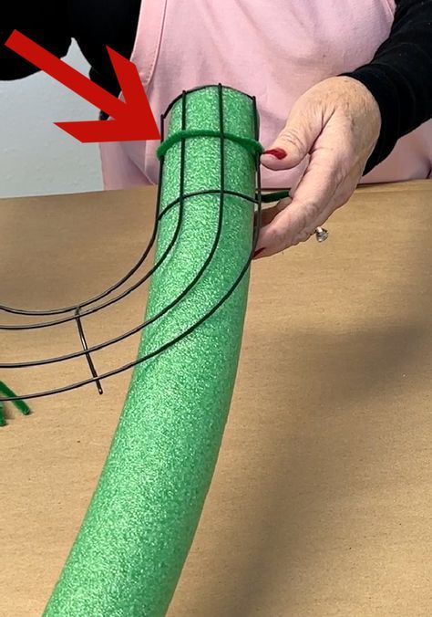 a person is making a green object out of paper and some wire with red arrows pointing to it