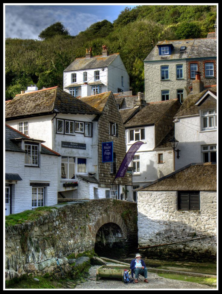 some people are sitting on the side of a river by buildings and a stone bridge