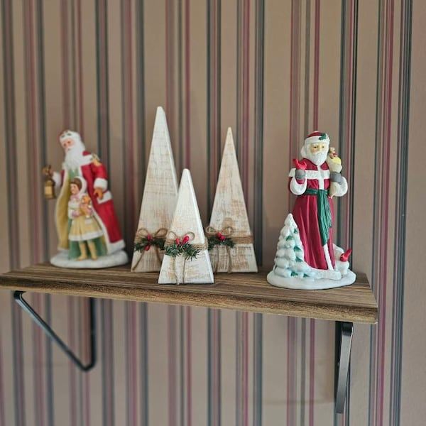 three christmas figurines sitting on top of a wooden shelf next to a striped wall