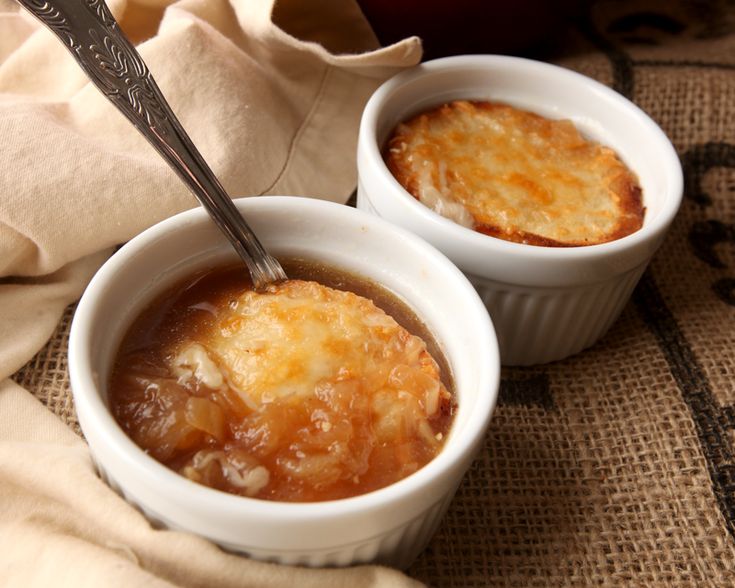 two small white bowls filled with food on top of a cloth covered table next to a napkin