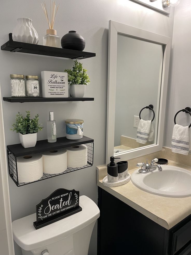 a white toilet sitting under a bathroom mirror next to a black shelf filled with towels