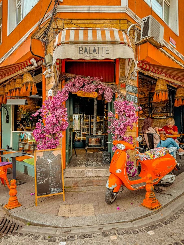 an orange scooter is parked in front of a building with flowers on it