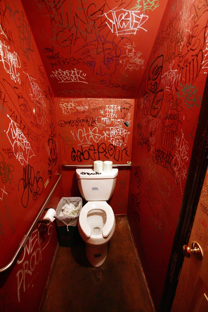 a toilet with graffiti all over it in a bathroom that has red walls and brown floors