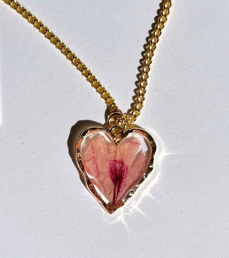 a necklace with a heart shaped pendant on a gold chain that has a pink flower in it