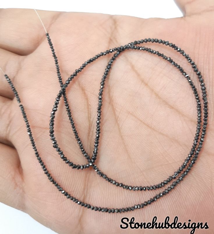 a hand holding a long black beaded necklace