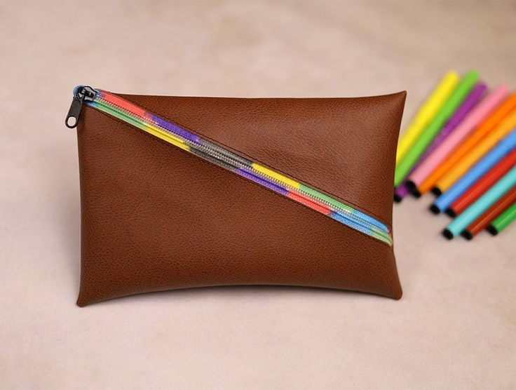 a brown leather pouch with colored pencils in it next to a pile of pens