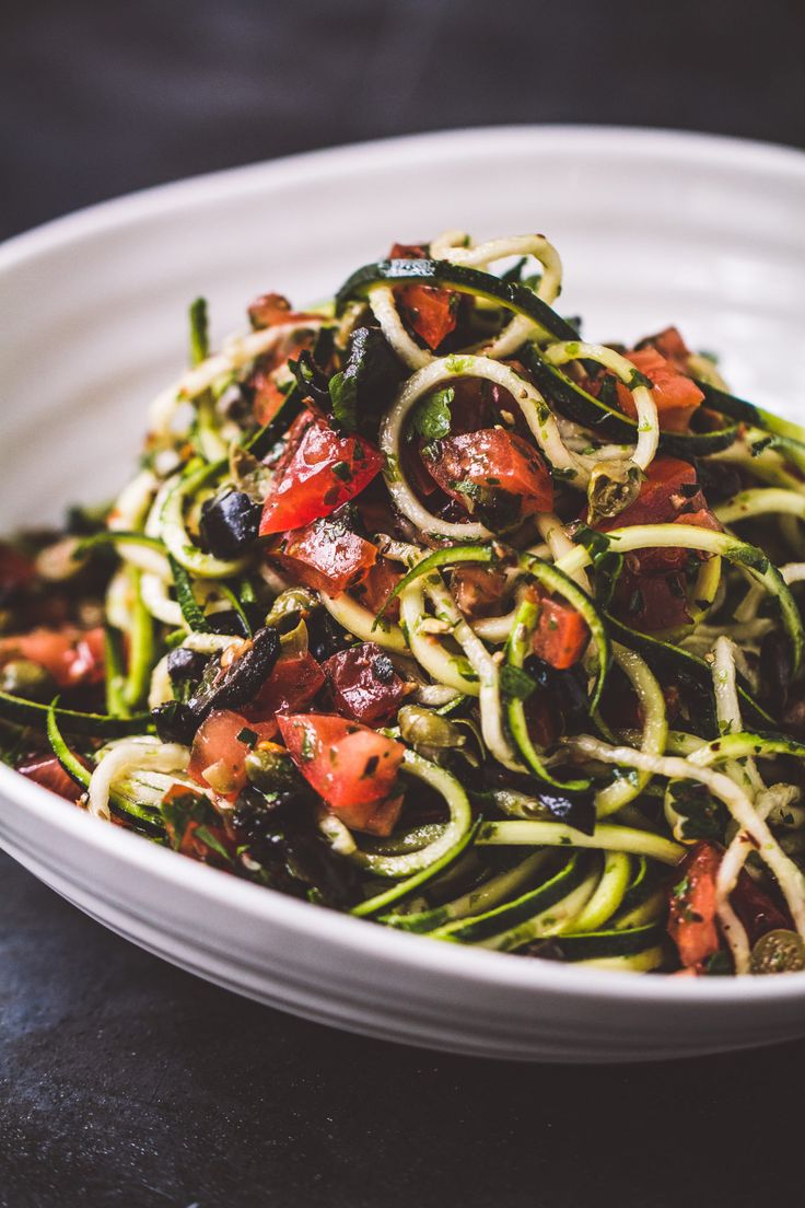 a white bowl filled with zucchini noodles and tomatoes on top of a table