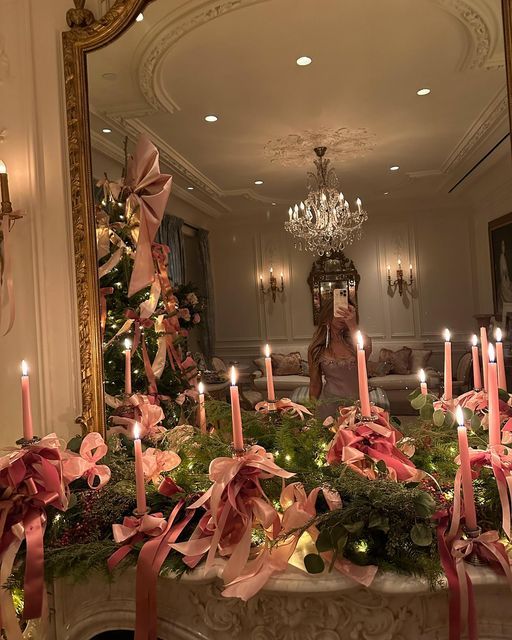 candles are lit in front of a christmas tree with pink ribbons and bows on it