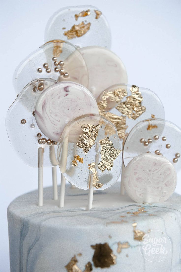 a white cake topped with lots of gold and frosted lollipops next to each other