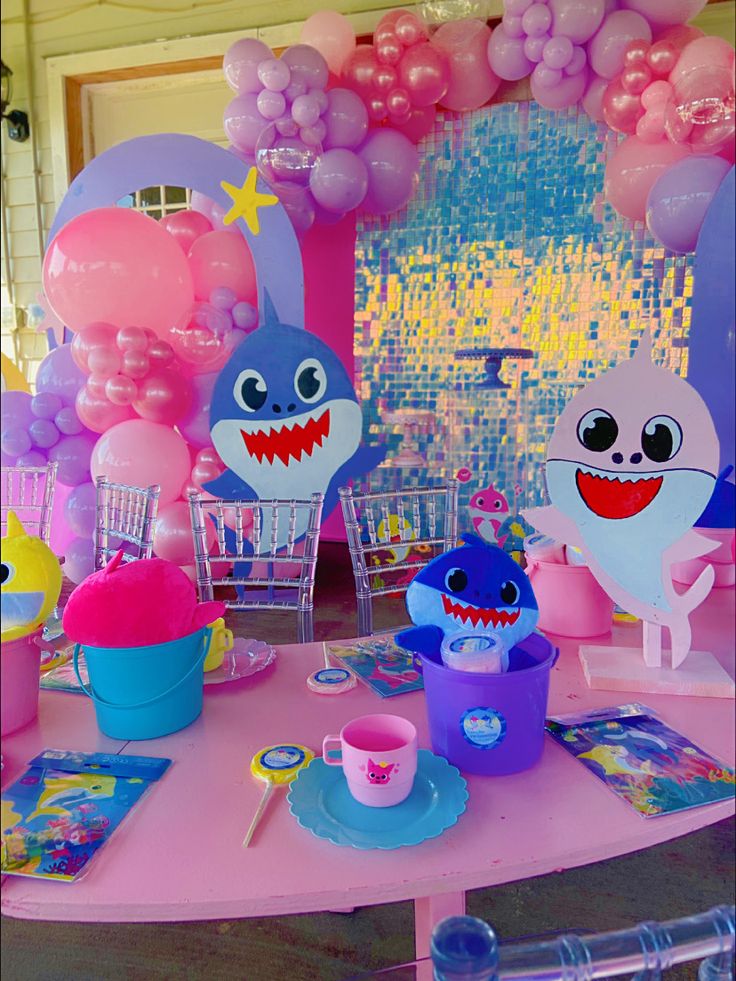 a pink table topped with balloons and shark decorations