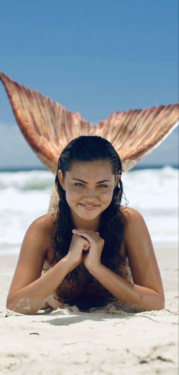 a beautiful woman laying on top of a sandy beach under a giant fish wings tail