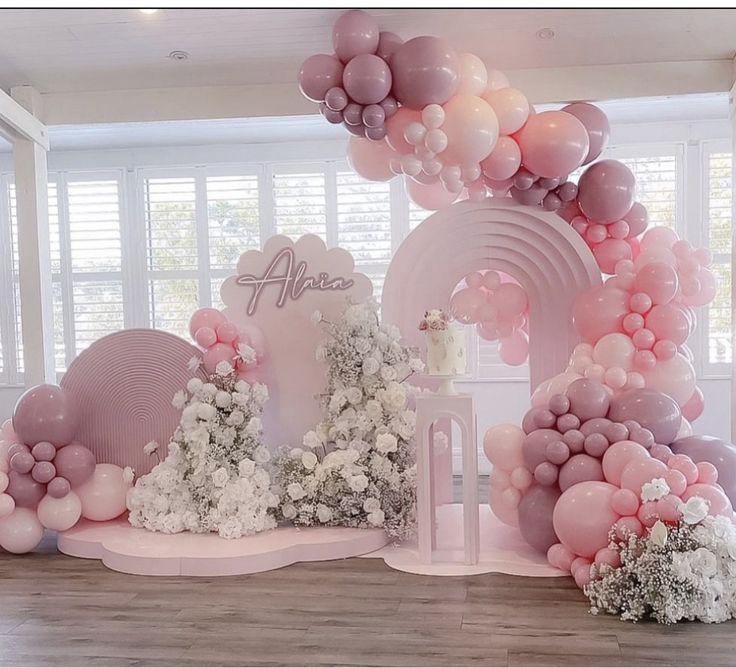 a pink and white balloon arch with flowers on the side for an elegant baby's first birthday party