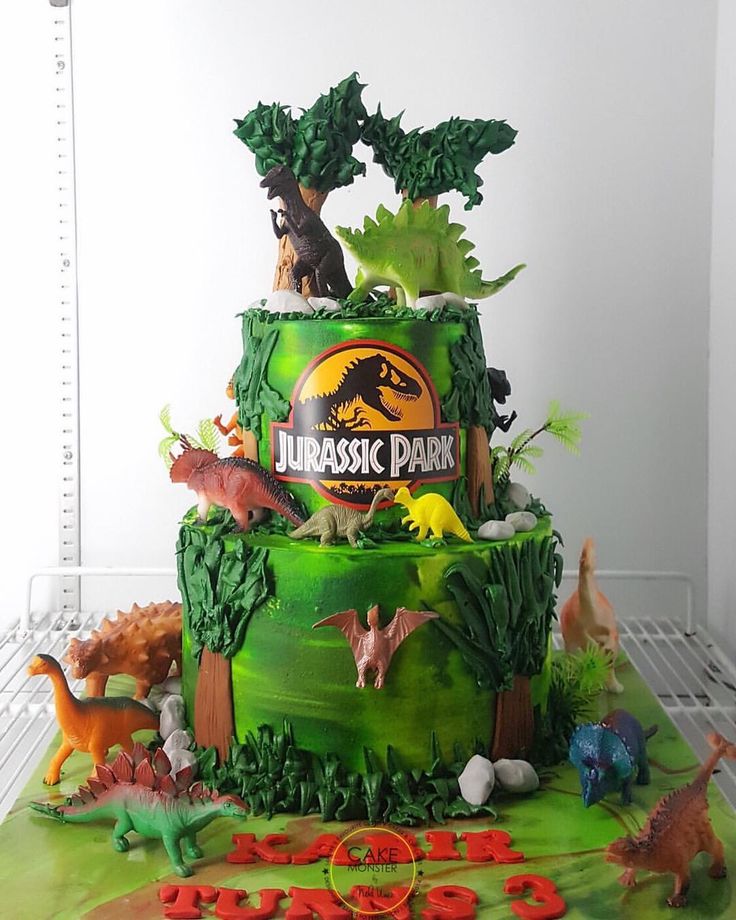 there is a green cake decorated with dinosaurs and plants on it's side,