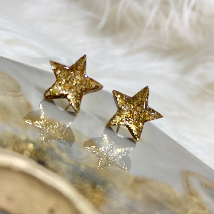 These resin star stud earrings are the perfect addition to your look. Featuring a glittery gold finish, these earrings have 18K gold plated and nickel free posts Trendy Gold Earrings With Star Charm, Gold Sparkling Earrings Gift, Sparkling Gold Earrings Gift, Trendy Gold Glitter Earrings, Trendy Glitter Gold Earrings, Gold Star-shaped Earrings For Party, Gold Glitter Jewelry Gift, Gold Glitter Jewelry As Gift, Gold Glitter Jewelry For Gifts