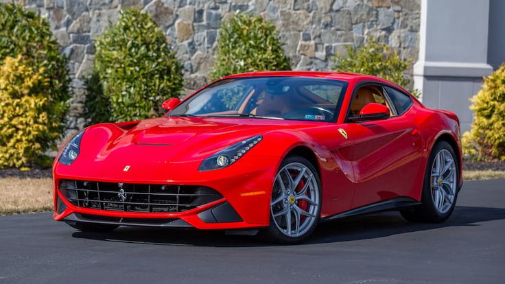 a red sports car parked in front of a stone wall and shrubbery behind it