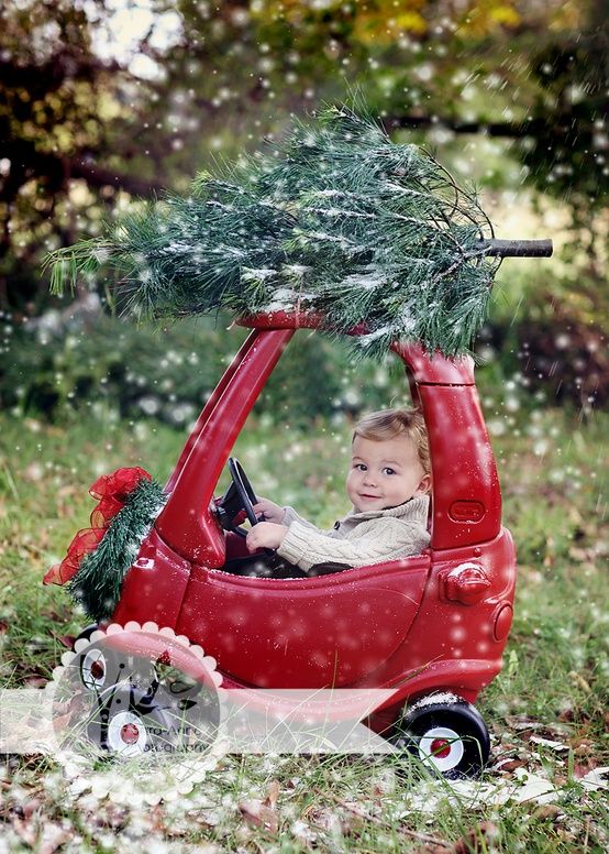 a little boy driving a red car with a christmas tree on the roof and steering wheel