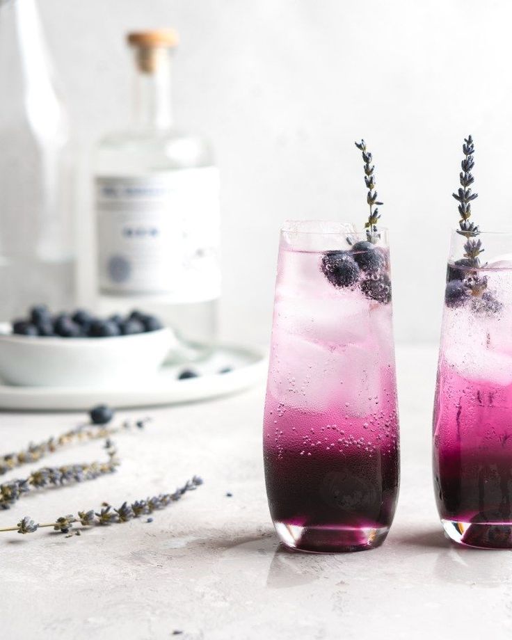 two glasses filled with blueberries and lavender spritkles next to a bottle of gin