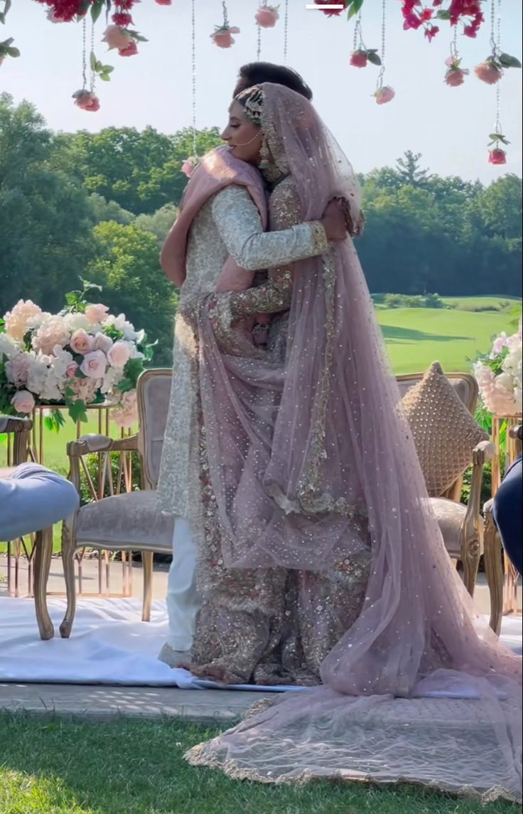 two people standing next to each other in front of a wedding arch with flowers hanging from the ceiling