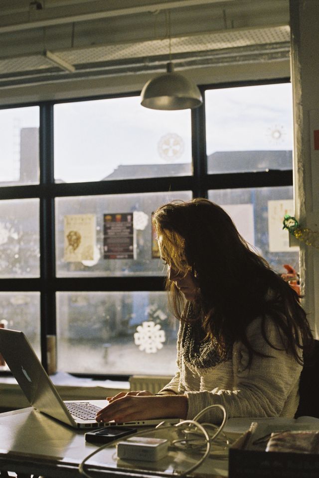 a woman sitting in front of a laptop computer on top of a desk next to a window