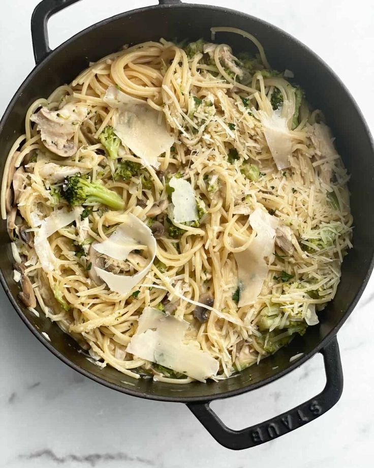 a pan filled with pasta and broccoli on top of a white marble counter