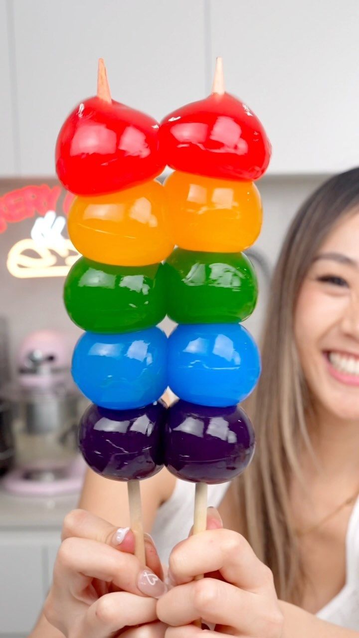 a woman holding up a rainbow colored lollipop