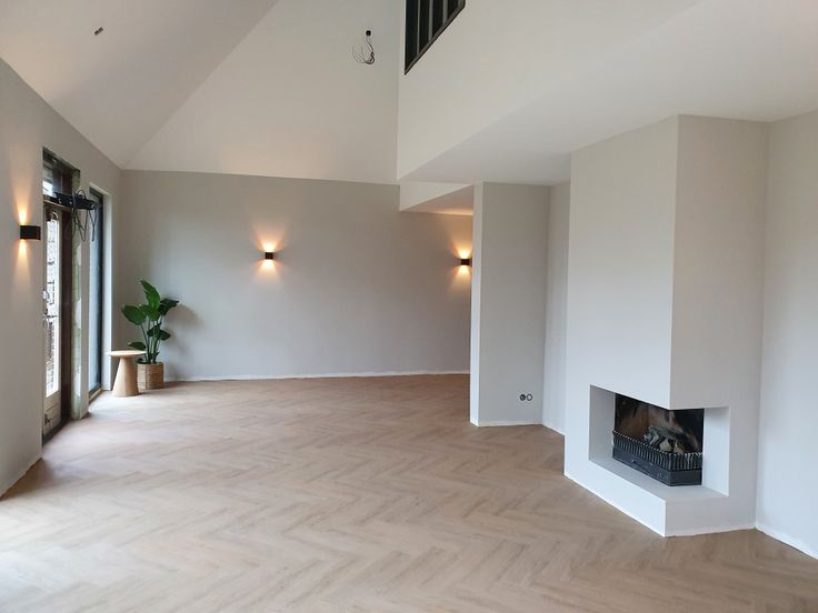 an empty room with white walls and wood flooring is seen in this image, there are lights on either side of the fireplace