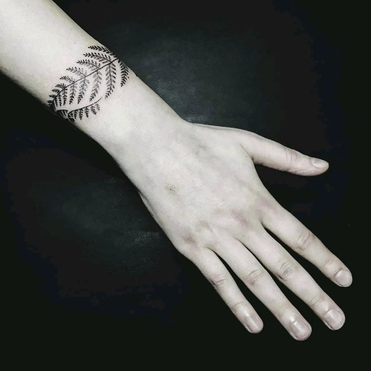 a person's hand with a black and white fern tattoo on the left wrist