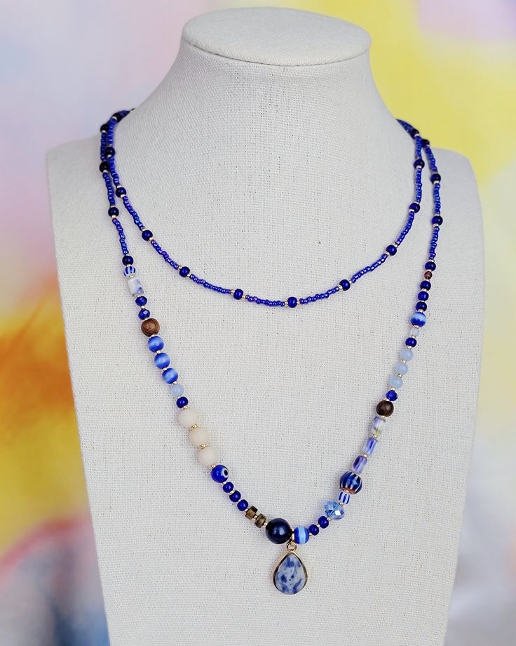 Handmade beaded necklace inspired by palm fronds against the blue sky. Long (34") clasp-free design allows for easy layering with other necklaces. This necklace features a stone pendant and beads of lapis lazuli, blue tiger's eye, wood, and millefiori glass. Blue Double Strand Spiritual Necklace, Bohemian Blue Lapis Lazuli Beaded Necklace, Blue Double Strand Gemstone Beaded Necklaces, Blue Gemstone Beads Jewelry For Layering, Blue Bohemian Long Necklace With Colorful Beads, Bohemian Blue Long Necklace With Colorful Beads, Blue Beaded Chain Spiritual Necklace, Bohemian Lapis Lazuli Beaded Necklace With Adjustable Fit, Bohemian Long Blue Necklace With Colorful Beads