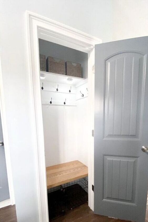 an open door leading to a mudroom with a bench on the floor and storage bins behind it