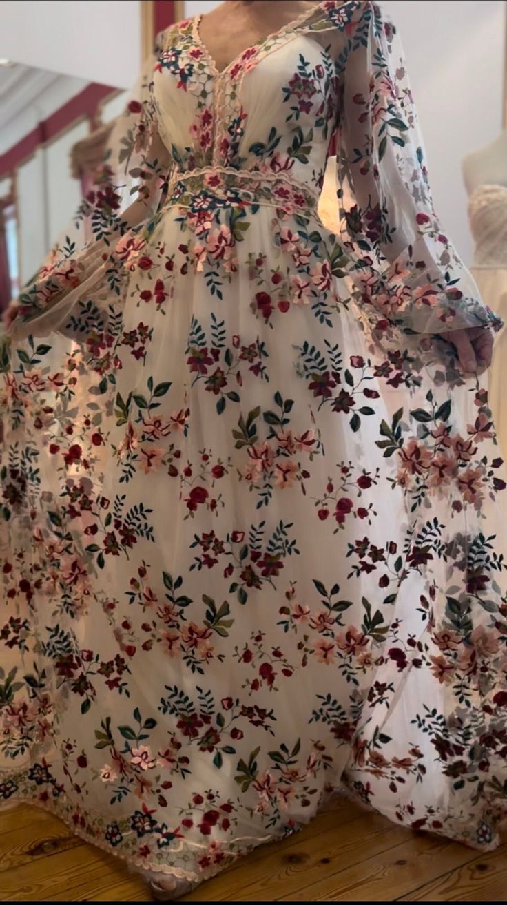 a woman in a white floral dress standing on a wooden floor next to a mannequin