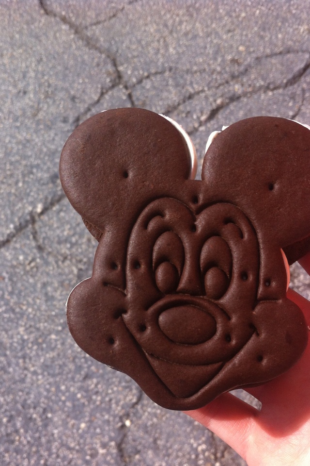 a hand holding a mickey mouse cookie with chocolate frosting on it's face