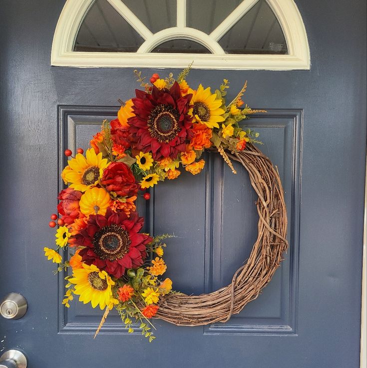 a wreath with sunflowers and other flowers is hanging on the front door's blue door